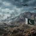 Photojournalistic image of geopolitical tension on the Pakistan-Afghanistan border. The background shows smoke rising from mountain villages amid an overcast sky. In the foreground, the Pakistani flag and the white Islamic Emirate of Afghanistan flag wave side-by-side on flagpoles. Military jets and a surveillance drone are visible in the sky.