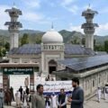 A mosque in Khyber Pakhtunkhwa with solar panels installed on its roof and minarets amidst news coverage and local observers.