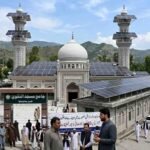 A mosque in Khyber Pakhtunkhwa with solar panels installed on its roof and minarets amidst news coverage and local observers.