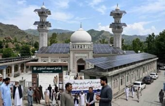 A mosque in Khyber Pakhtunkhwa with solar panels installed on its roof and minarets amidst news coverage and local observers.