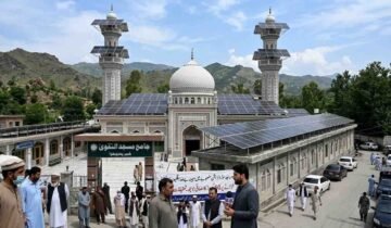 A mosque in Khyber Pakhtunkhwa with solar panels installed on its roof and minarets amidst news coverage and local observers.
