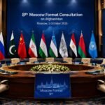 Empty diplomatic conference hall prepared for the 8th Moscow Format Consultation on Afghanistan, with Pakistan, Russia, China, Iran, Tajikistan, Uzbekistan, the Islamic Emirate of Afghanistan and other participating flags displayed behind vacant chairs.
