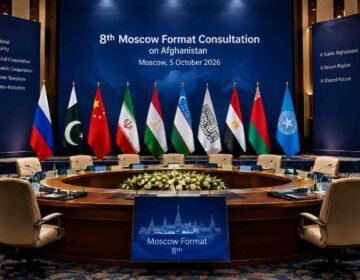 Empty diplomatic conference hall prepared for the 8th Moscow Format Consultation on Afghanistan, with Pakistan, Russia, China, Iran, Tajikistan, Uzbekistan, the Islamic Emirate of Afghanistan and other participating flags displayed behind vacant chairs.